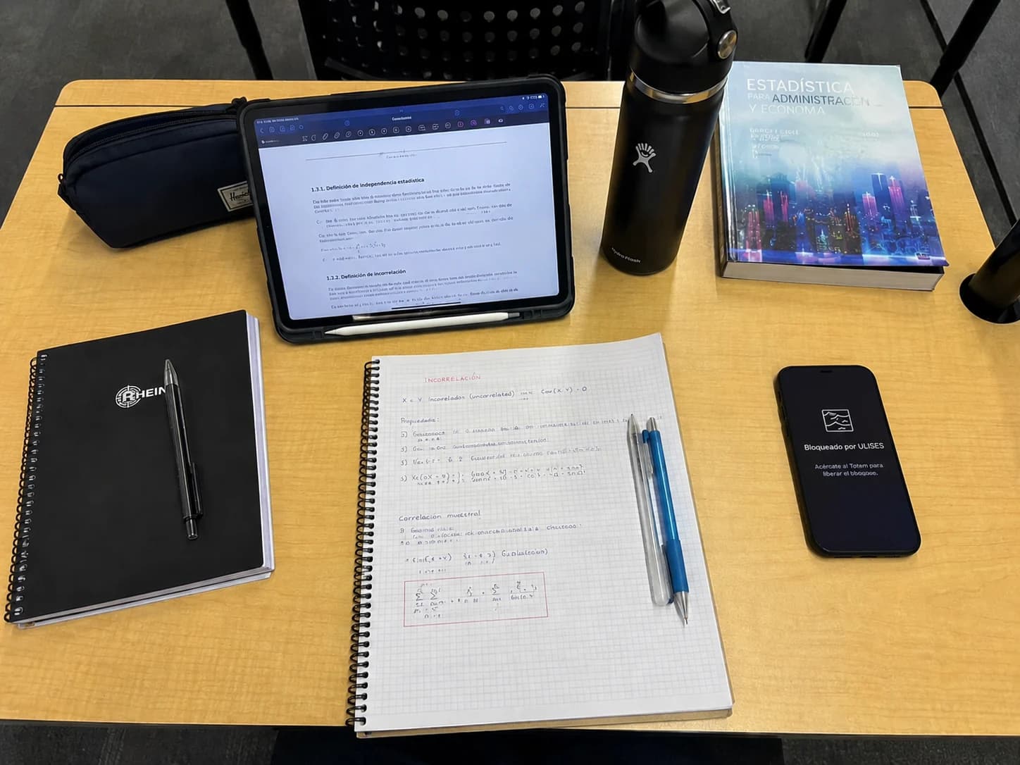 Escritorio de estudio: cuaderno, tablet con apuntes y el teléfono a un lado mostrando el bloqueo de ULISES.