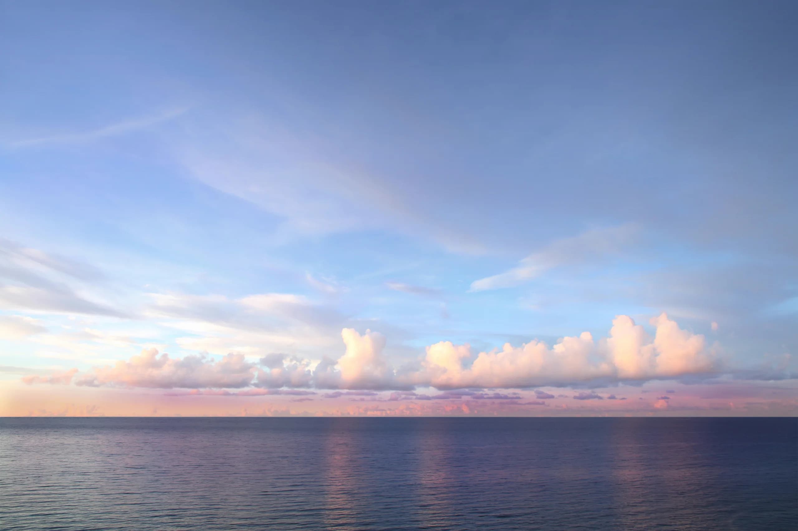 Horizonte de mar en calma al atardecer, con nubes bajas teñidas de rosa.
